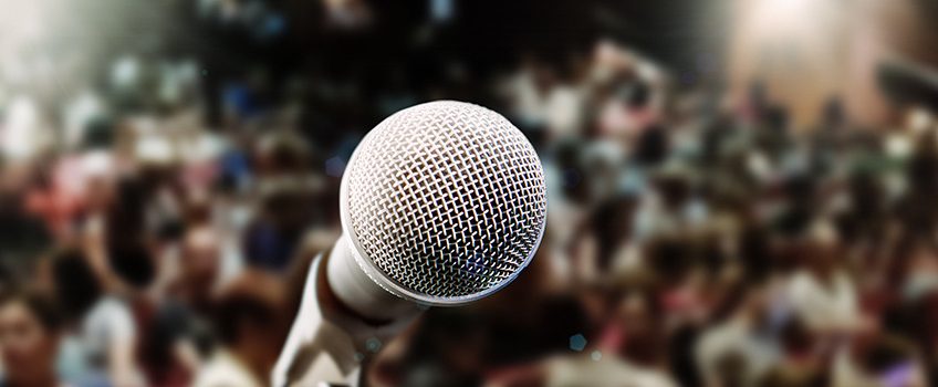 close-up-of-microphone-with-spot-lit-defocused-audience