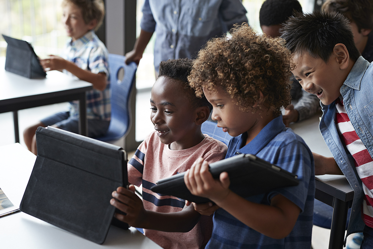 Tres chicos utilizan sus tablets en el aula. 