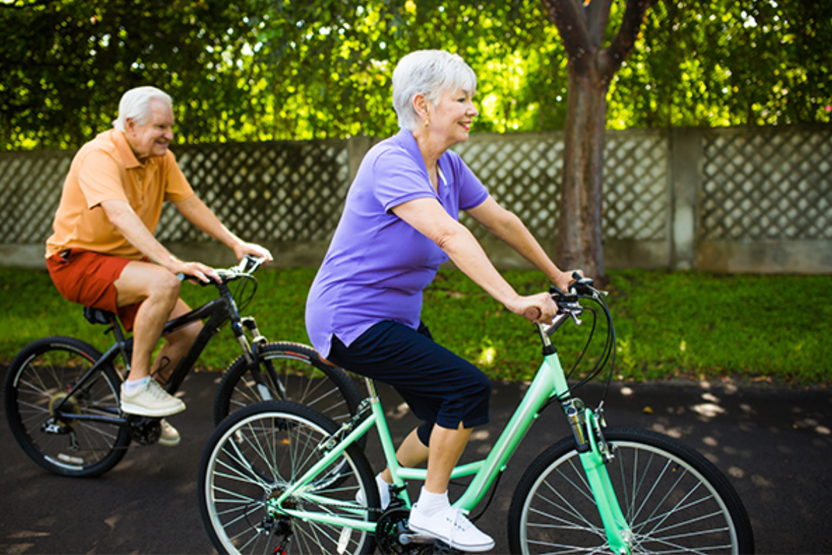 Dos adultos mayores haciendo ejercicio físico (manejando bicicleta) para mejorar su salud. 
