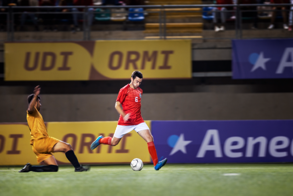 Jugadores de fútbol en un estadio con público de fondo. 
