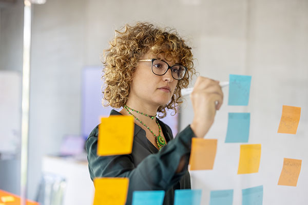 businesswoman-writing-on-adhesive-note-on-glass-wall-at-startup-workplace