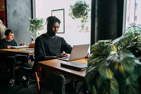 black-man-with-a-laptop-uses-artificial-intelligence-while-sitting-at-a-table-in-a-cafe-while-traveling