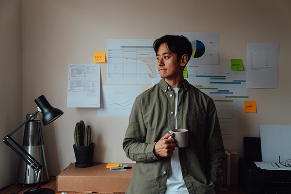 thoughtful-asian-man-taking-a-coffee-break-while-working-from-home